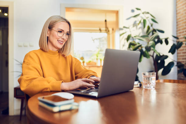 middle aged woman sitting at dinning with laptop